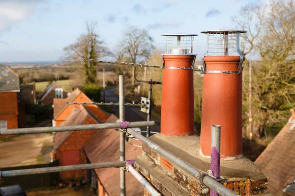 Clay chimney pot with cowl on a roof, repairing chimney with scaffolding UK