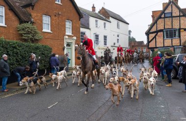 WINSLOW, UK - December 26, 2018. Fox hunting, men in costume riding on horses with a pack of hounds through a rural town in Buckinghamshire, England clipart