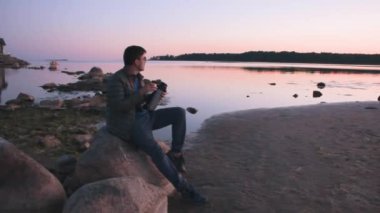 Genç adam kumsalda güneşin doğuşunu ve termos enerjisinden kahve yudumlamayı sever.