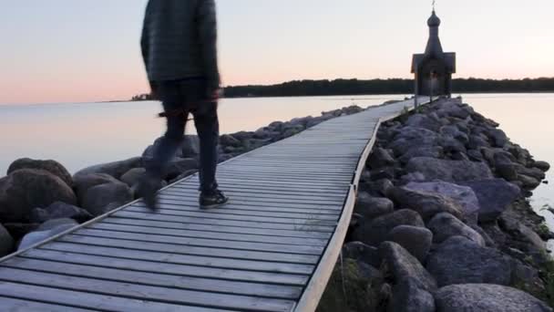 Man Loopt Een Pier Vanaf Houten Kerk Bij Zonsondergang Kalm — Stockvideo