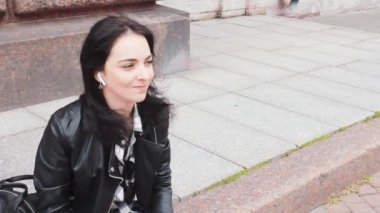 Genç ve çekici bir kız dans ederken kaldırımda neşeli bir şekilde oturuyor.