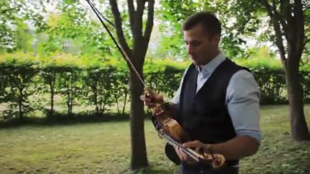 Violinista joven camina por el parque y toca — Vídeos de Stock
