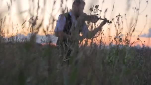 Silhueta jovem de um violinista no campo ao pôr do sol tocando violino — Vídeo de Stock