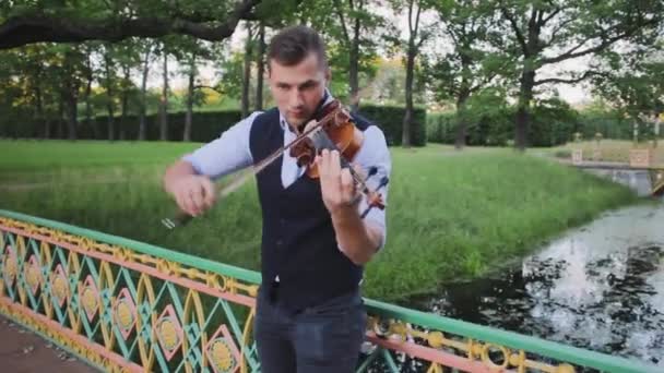 Violinista joven en el parque público en el puente tocando el violín — Vídeos de Stock