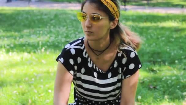 Mode meisje hipster zitten op het gazon in het park en denkt — Stockvideo
