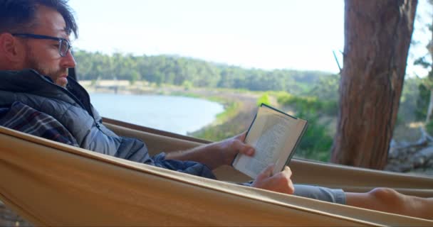 Άνθρωπος Διαβάζοντας Ένα Βιβλίο Ενώ Χαλαρώνετε Μια Αιώρα Μια Ηλιόλουστη — Αρχείο Βίντεο