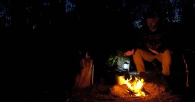 Gece 4 k ormanda kamp ateşi yanında oturan adam