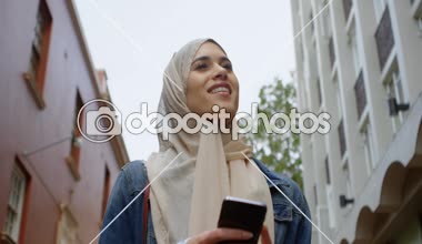 Sokak 4 k üzerinde yürürken cep telefonuyla hijab mutlu kadın