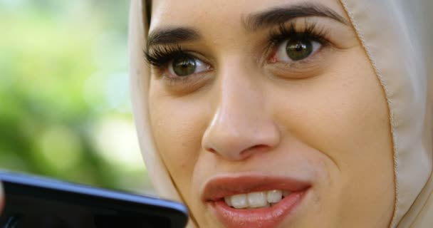 ヒジャーブ ガーデン で携帯電話を使用しながら笑顔の女 — ストック動画