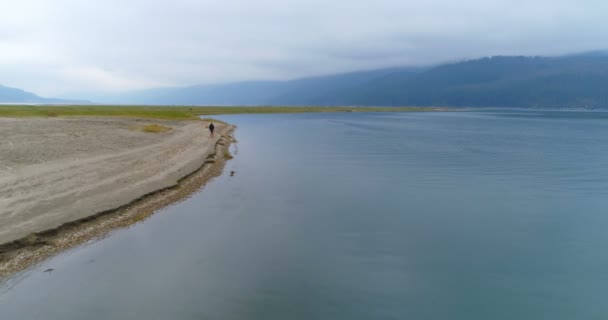 で湖畔に近い彼の犬を連れて歩いて男 — ストック動画