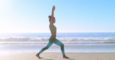 Güneşli bir günde 4 k kumsalda Yoga gerçekleştirme kadın