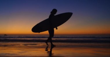 Kadın sörfçü surfboard ile 4 k gün batımında sahilde yürüyüş