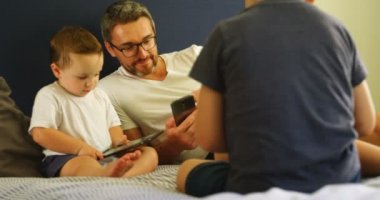 Baba ve çocuklar üzerinde cep telefonu ve dijital tablet kullanarak evde 4 k yatak