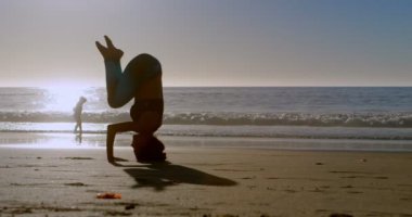 Güneşli bir günde 4 k kumsalda Yoga gerçekleştirme kadın uygun
