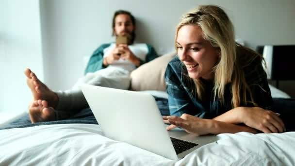 快乐夫妇使用笔记本电脑和手机在床上在家里4K — 图库视频影像