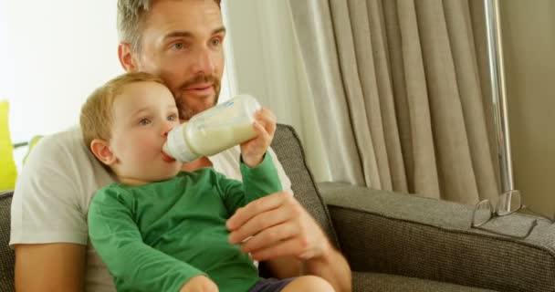 の自宅のソファの上のミルクを飲む父周に座っている男の子 — ストック動画