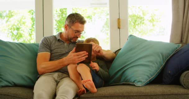 父亲和儿子使用数码片在沙发上的家庭4K — 图库视频影像