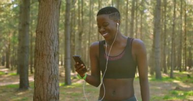 Gülümseyen kadın jogger cep telefonuyla ormanda 4 k