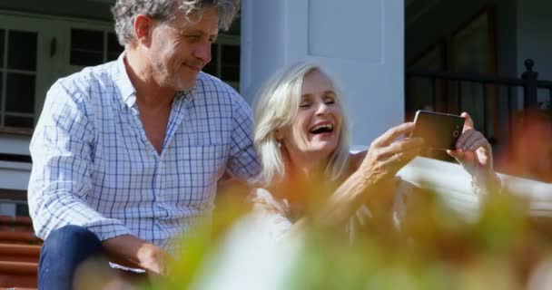 のベランダで携帯電話を使用して幸せな先輩カップル — ストック動画