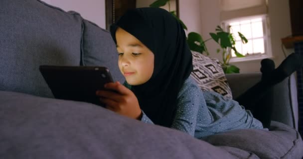ヒジャーブ ホーム でリビング ルームでデジタル タブレットを使用しての女の子 — ストック動画