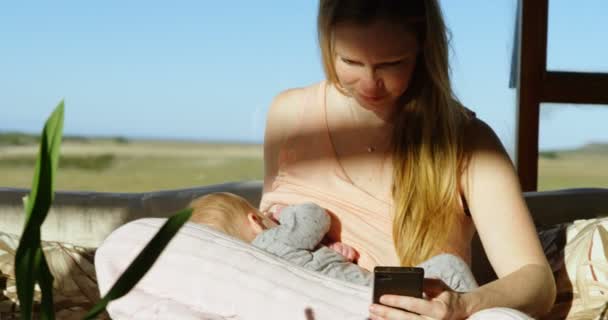 Moeder Met Behulp Van Mobiele Telefoon Tijdens Borstvoeding Aan Haar — Stockvideo
