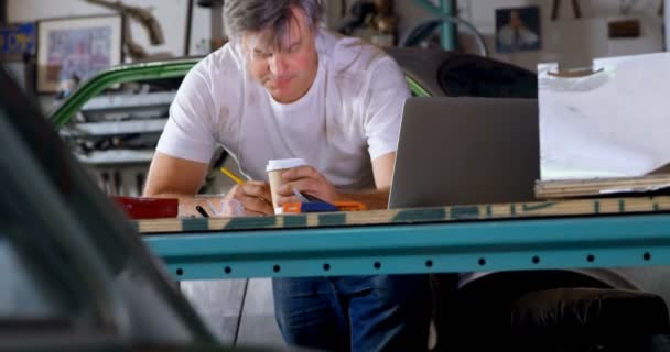 男技工在4K 车库桌上写字时喝咖啡 — 图库视频影像