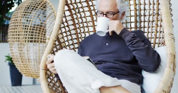 Senior Man Having Coffee While Reading A Book In Hanging Chair 4k