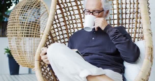 Älterer Mann Beim Kaffee Während Hängesessel Ein Buch Liest — Stockvideo