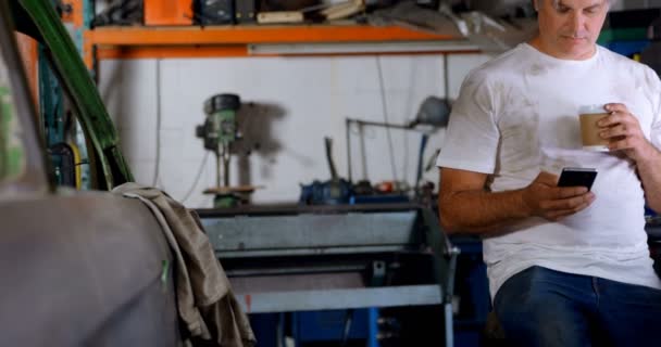 Male Mechanic Having Coffee While Using Mobile Phone Garage — Stock Video