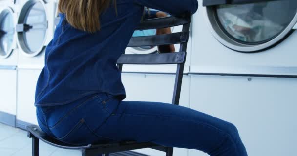 坐在自助洗衣店的椅子上的美丽的女人4K — 图库视频影像