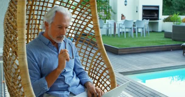 Старший Чоловік Використовує Ноутбук Сидячи Підвішеному Кріслі Біля Басейну — стокове відео