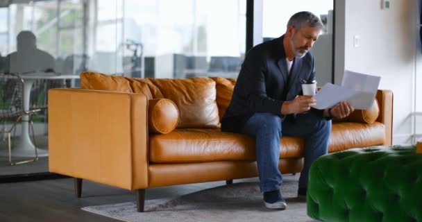 商人与咖啡杯检查文件在沙发上的办公室4K — 图库视频影像