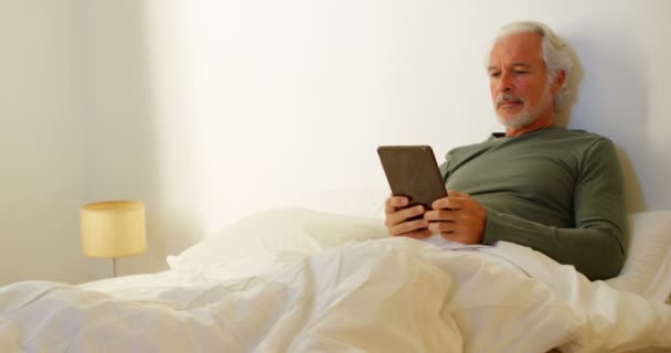 年配の男性が寝室でベッドの上ホーム デジタル タブレットを使用して — ストック動画