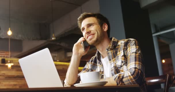 Hombre Joven Hablando Teléfono Móvil Mientras Usa Ordenador Portátil Cafetería — Vídeos de Stock