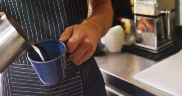 のカフェでマグカップにミルクを注ぐ男性ウェイターの半ばセクション — ストック動画