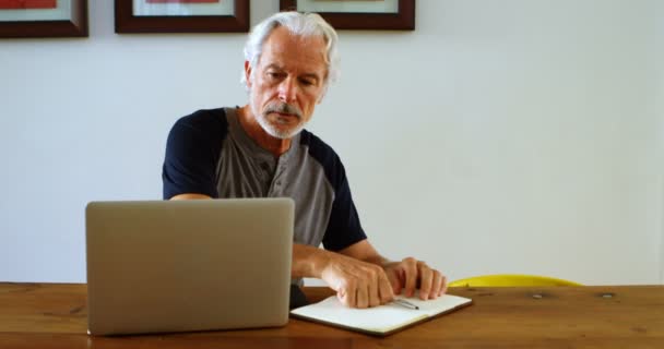 Senior Mann Schreibt Auf Notizblock Auf Tisch Hause — Stockvideo