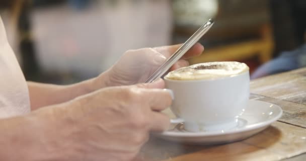 のカフェで携帯電話を使用しながらコーヒーを飲んでいる年配の女性の中央部 — ストック動画