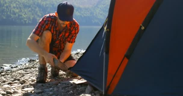 Молодой Человек Готовит Палатку Возле Реки — стоковое видео