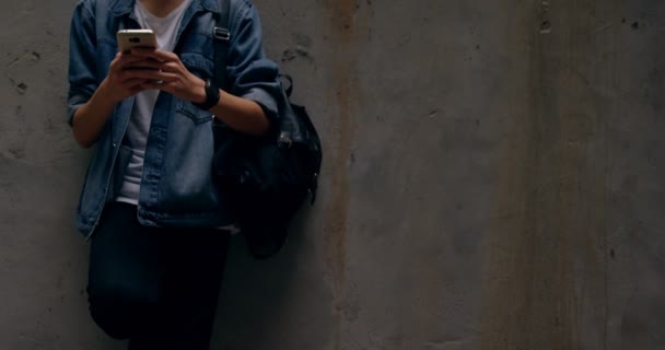 の壁にもたれながら携帯電話を使用して若い男 — ストック動画