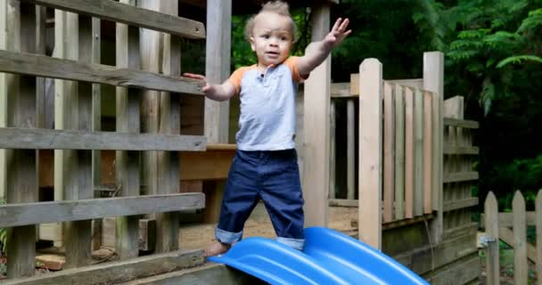 の裏庭で再生の家でスライドの近くに立っている男の赤ちゃん — ストック動画