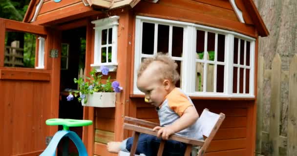 小男孩坐在椅子附近玩房子在后院4K — 图库视频影像