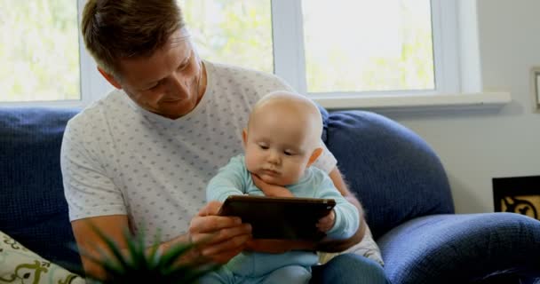在家里的客厅里使用数字平板电脑的爸爸和男婴4K — 图库视频影像