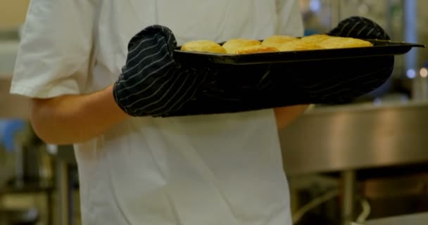 年轻的男性厨师在厨房里闻着饼干托盘 — 图库视频影像