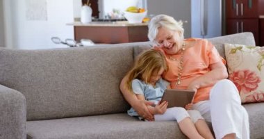 Büyükanne ve torunu dijital tablet oturma odasında ev 4 k kullanma.
