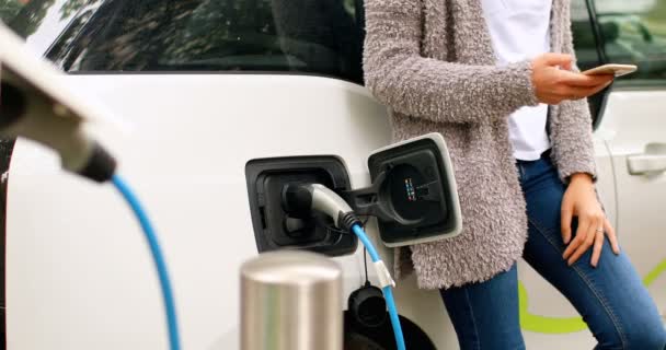 Mittelteil Der Frau Nutzt Handy Beim Laden Von Elektroauto Ladestation — Stockvideo