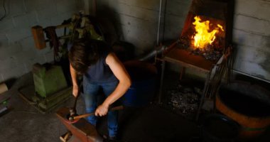 Bir kadın metal fabrikasında parlayan sıcak nal kalıplama yüksek açı bakış. Bir çekiç ve keski ile ateş içinde belgili tanımlık geçmiş ile vurmaya.