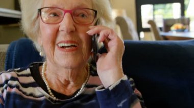 Cep telefonu evde oturma odasında kanepede otururken konuşurken gözlüklü bir üst düzey emekli kadın yakın çekim.