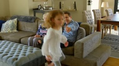 Mutlu bir aile evde oturma odasında eğleniyor. Küçük kız ablasını büyük annesi ve babası ile tablo aşağı atlama izliyor.
