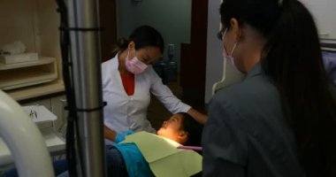 Özenli kadın Asya dişçi randevunuz klinikte Genç hastada ile etkileşim beyaz önlük giyen yan görünüm