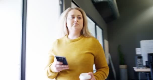 美しい金髪のビュー角度を低実業家ウォーキング コーヒーを飲みながら オフィスで携帯電話を使用して 同僚の多民族のグループはラップトップに取り組んでいます — ストック動画